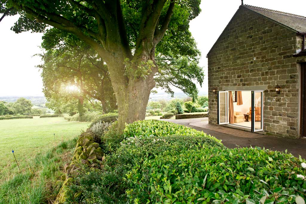 a newbury countryside brown brick building with open white aluminium bifold doors next to a field and lush green trees